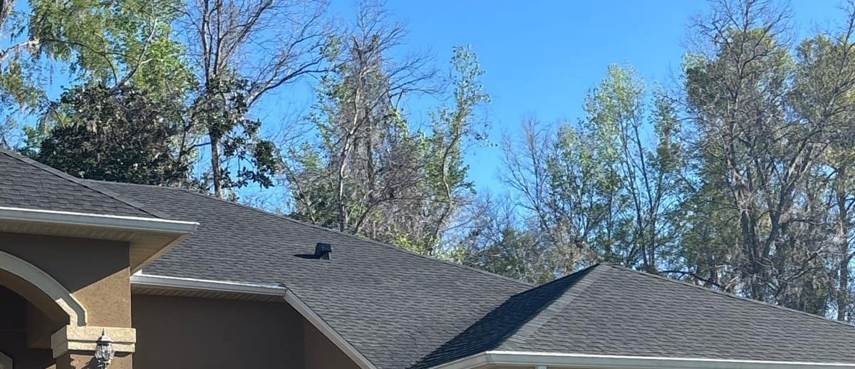 Front of the Alachua home: stucco entry, white fascia and new hip roofs under tall trees