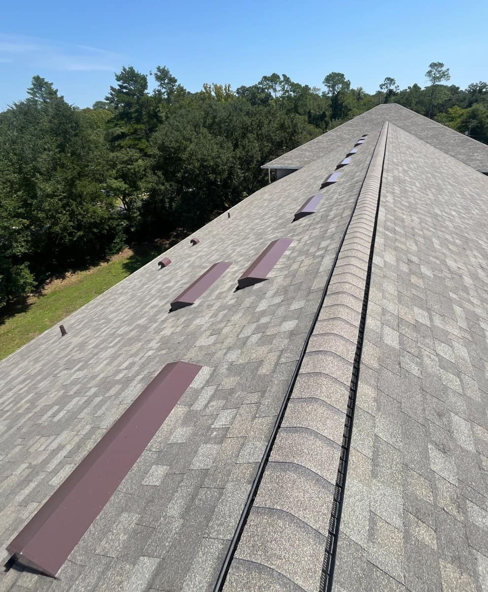 Ridge vent under ridge cap shingles beside a line of box vents on the Gainesville roof