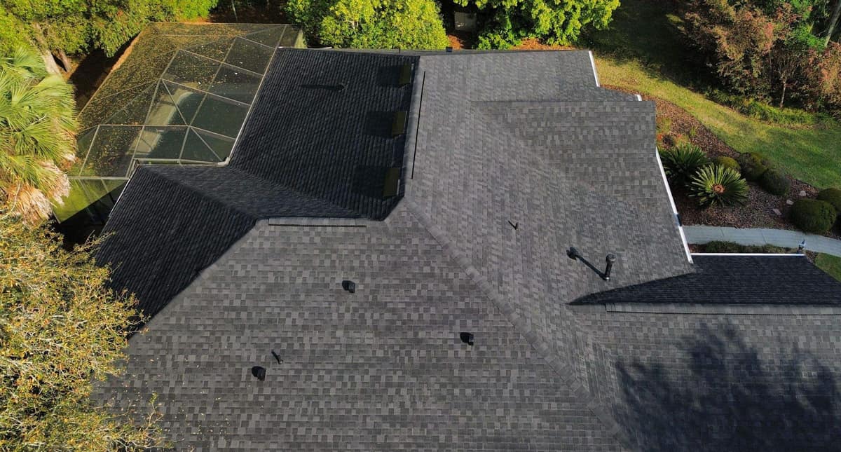Drone view looking down on the new dark gray shingle roof and screened enclosure of a Gainesville home