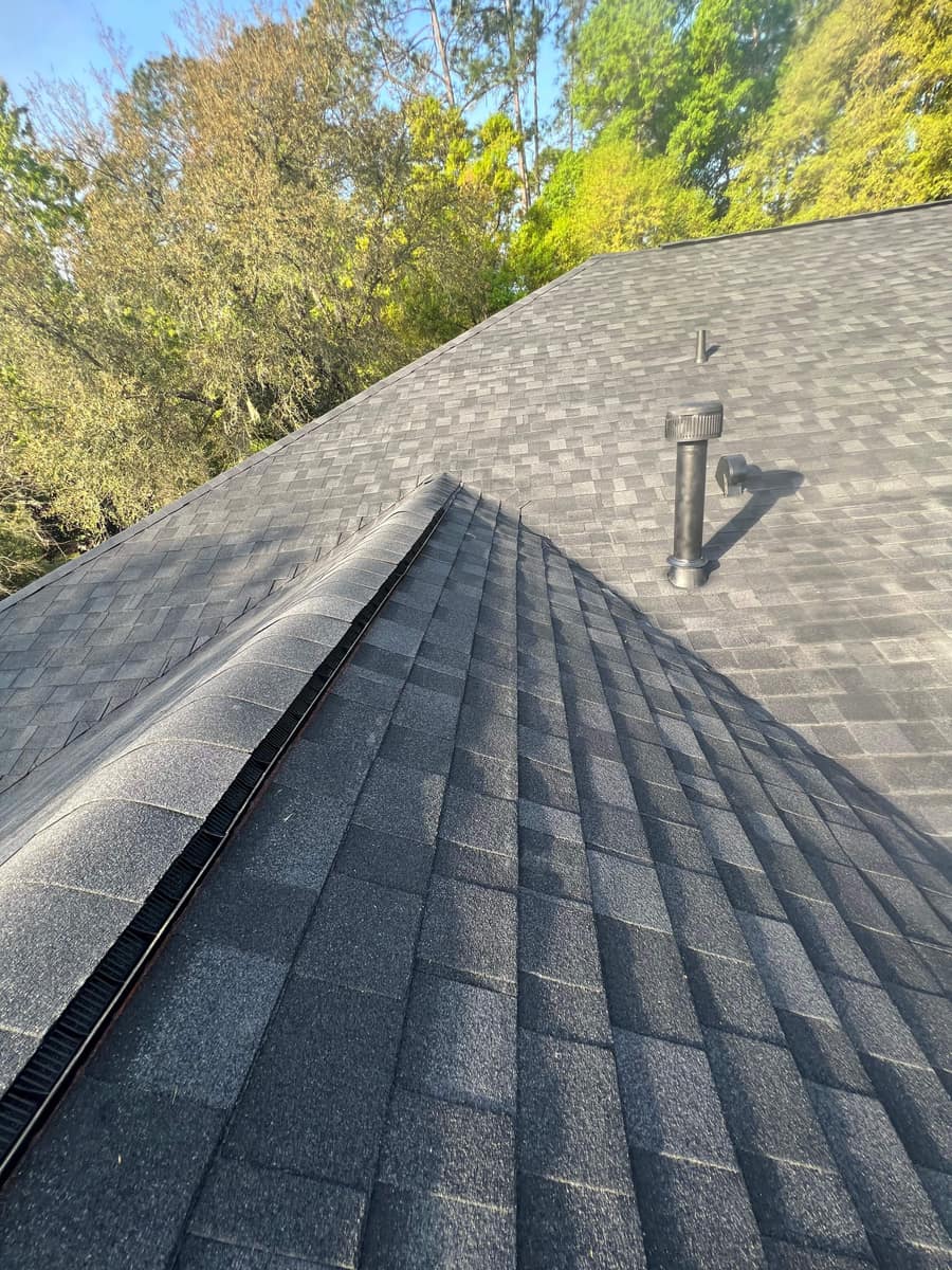 Ridge vent under capped shingles on the gable wing of the Gainesville roof, black vent stack behind