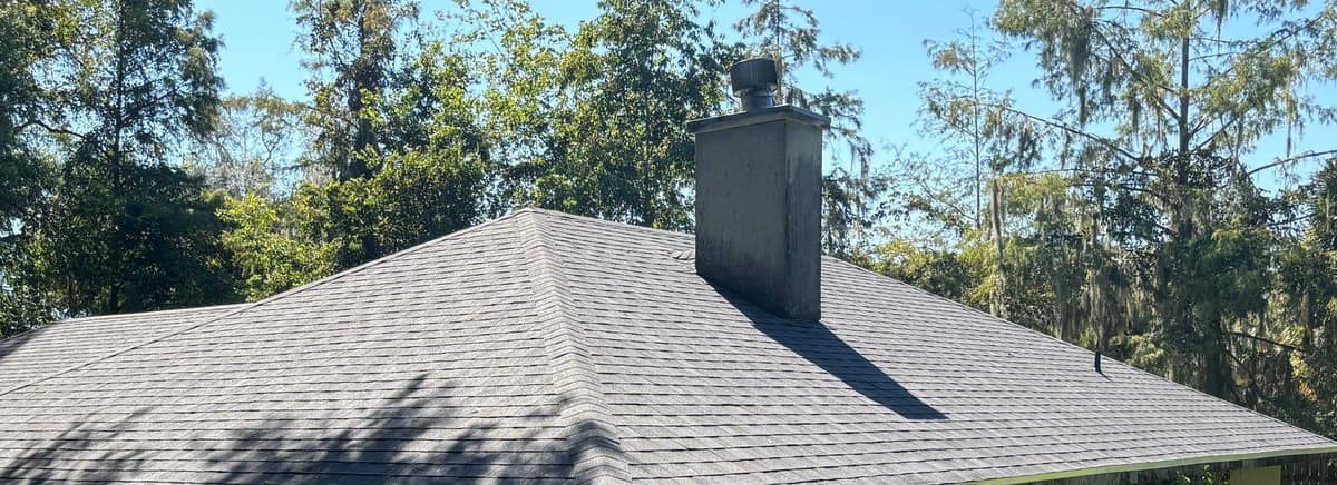 Stucco chimney with a round metal cap rising from the new gray shingles in Gainesville