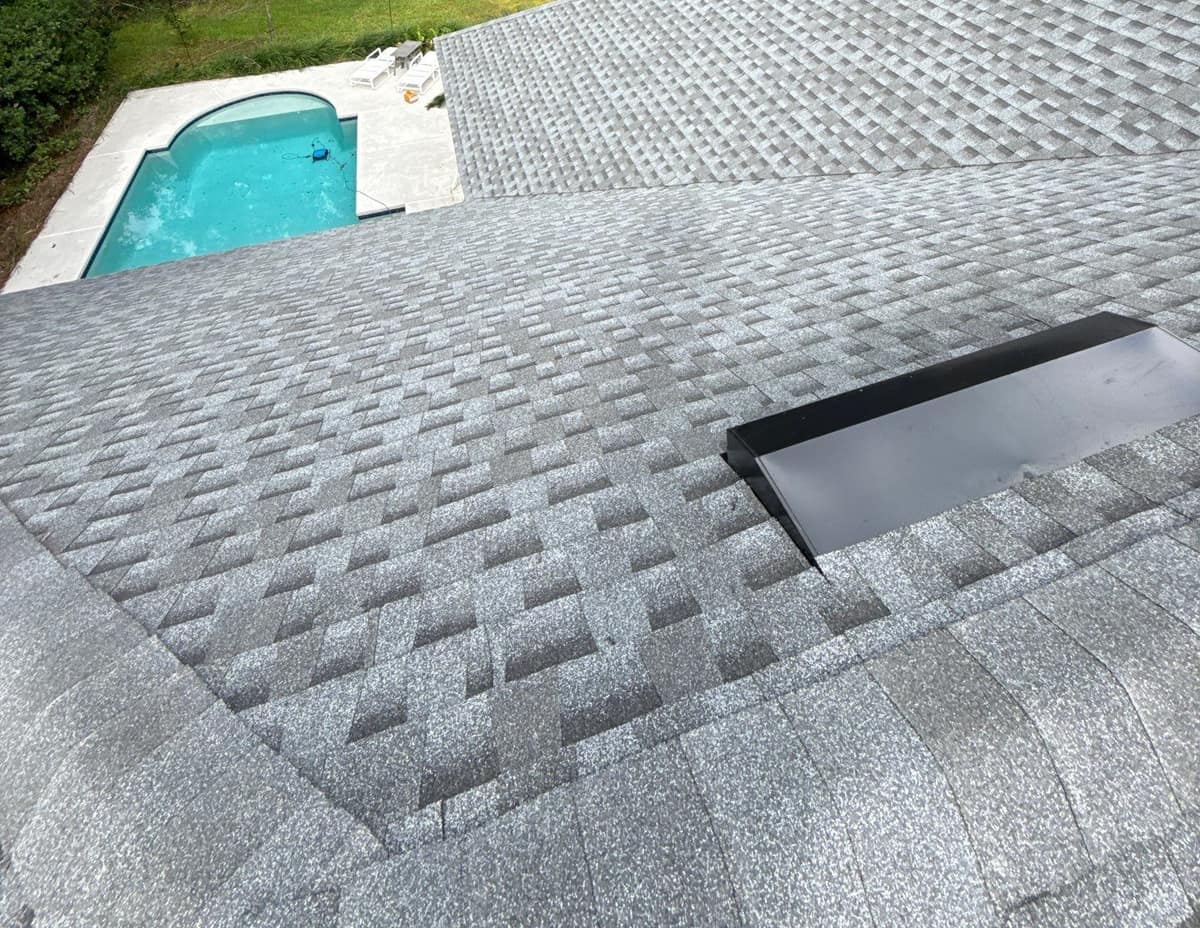 Roof-level view across new light gray architectural shingles toward the backyard pool of a Gainesville home