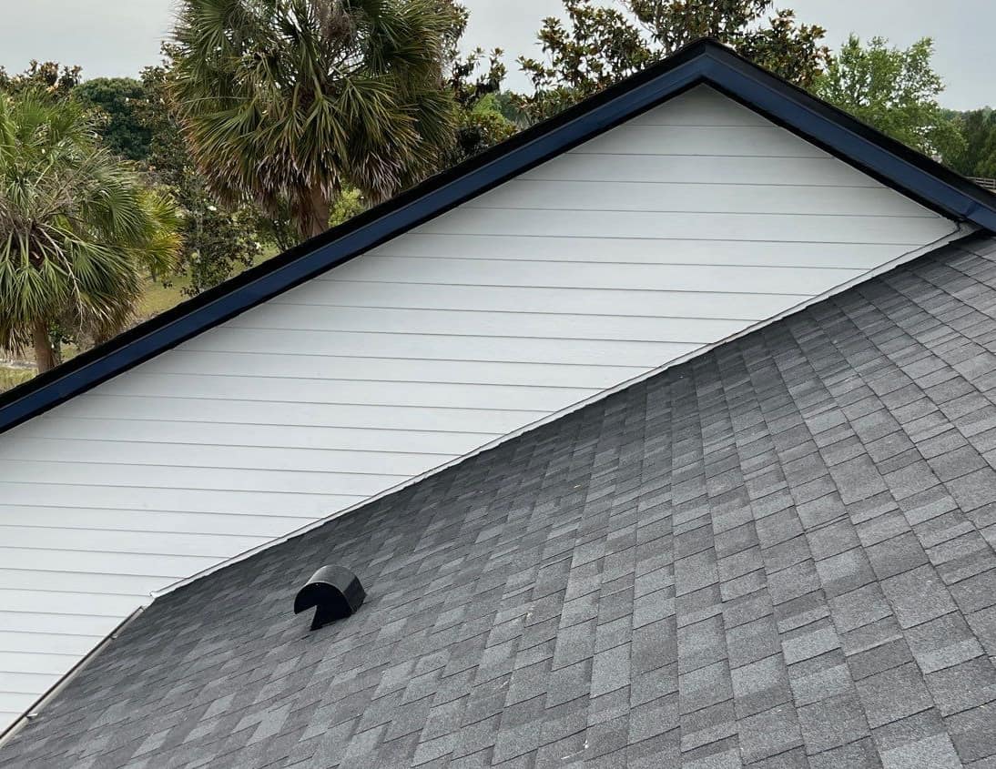 White sided gable with navy rake trim above new gray shingles and a hooded vent in Gainesville