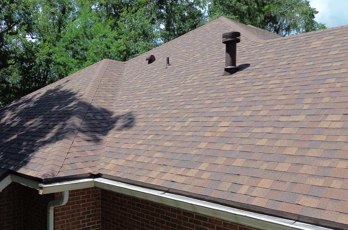 Tall flue pipe, goose-neck vent and brown drip edge above a white gutter in Gainesville