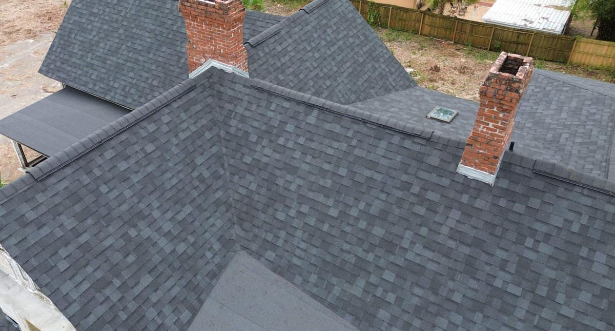 Drone view across the new charcoal gray roof and two brick chimneys of a Victorian-style Gainesville house