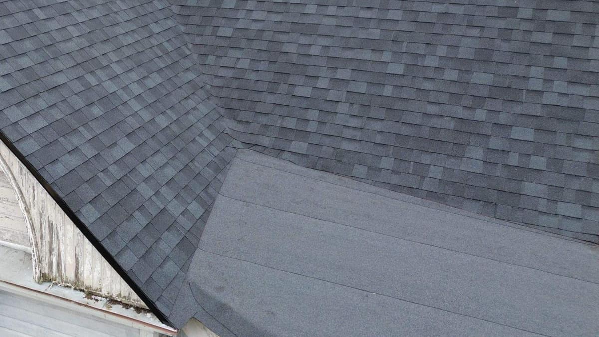 Black drip edge on the front gable rake next to a low-slope cap over a round bay
