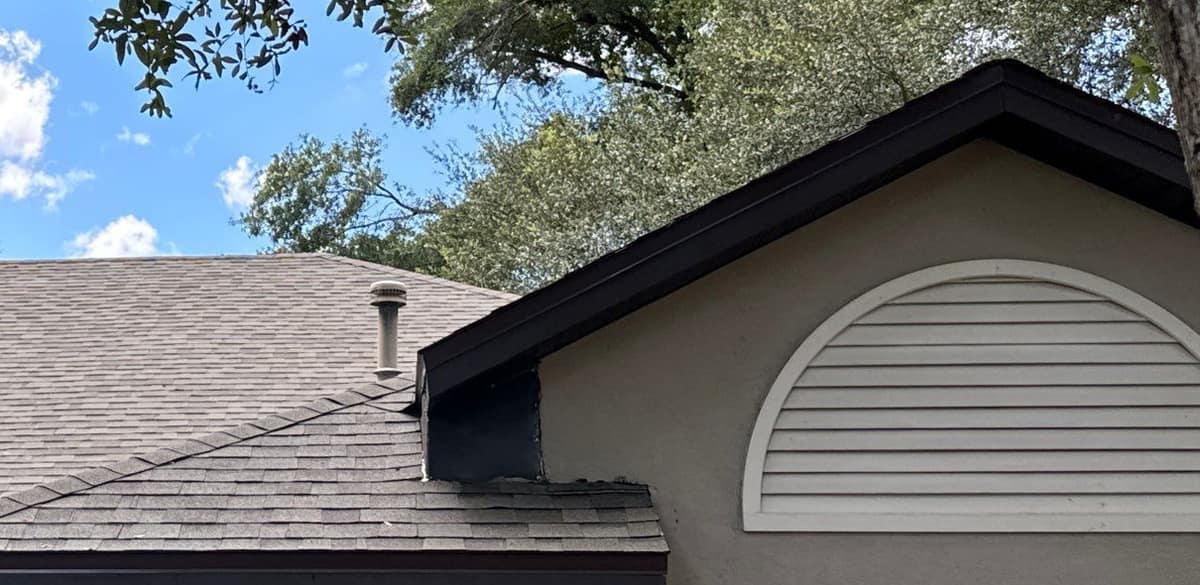 Dark metal flashing where a lower roof meets the gable wall beside a half-round louvered vent, Gainesville
