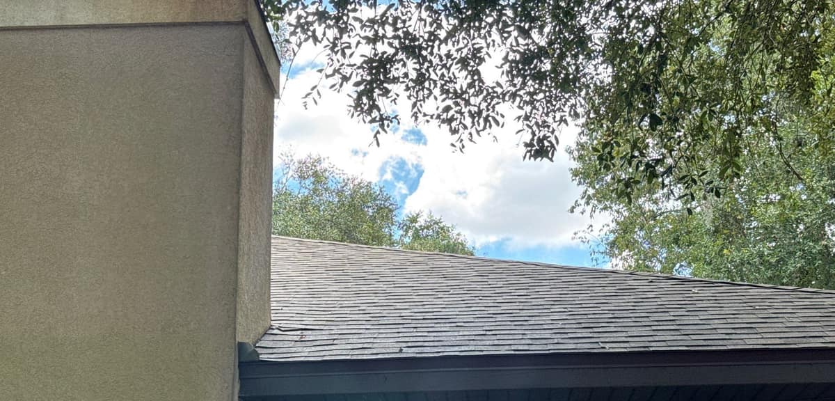 Stucco chimney chase standing beside the new shingles and dark brown fascia in Gainesville