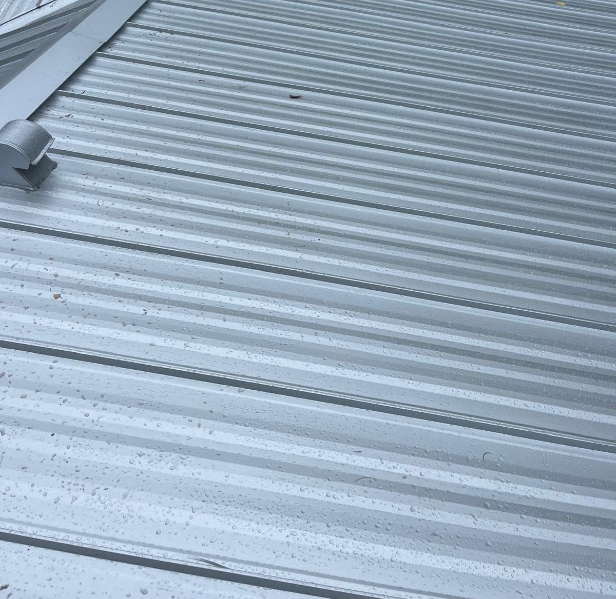 Ribbed metal panels beaded with water beside a hood vent and ridge cap in Hampton