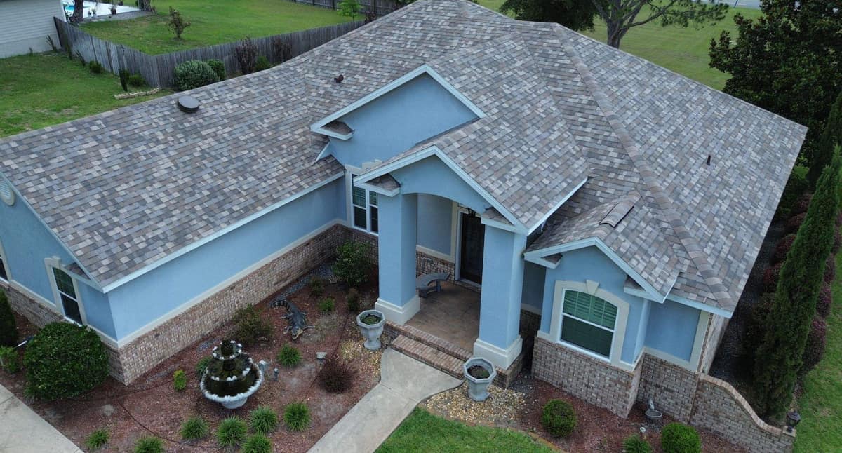 Drone view of a Lake City home with blue stucco walls under a new multi-tone shingle roof