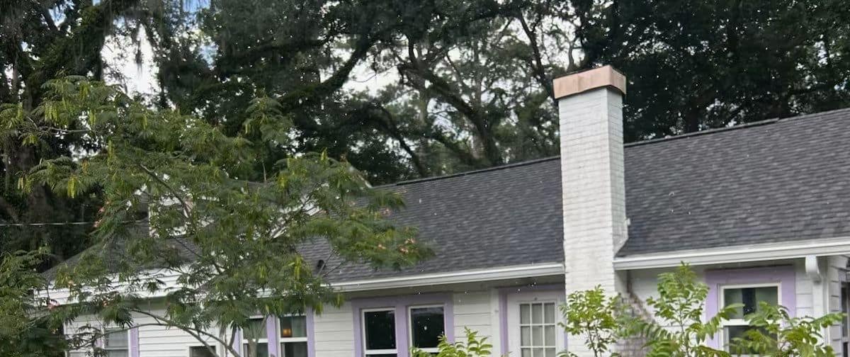 White cottage in Live Oak with a new gray shingle roof, a white brick chimney and lavender trim