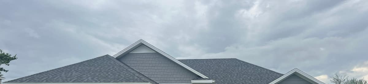 Front roofline of the Newberry home under heavy clouds, with a tall gable faced in gray shake siding