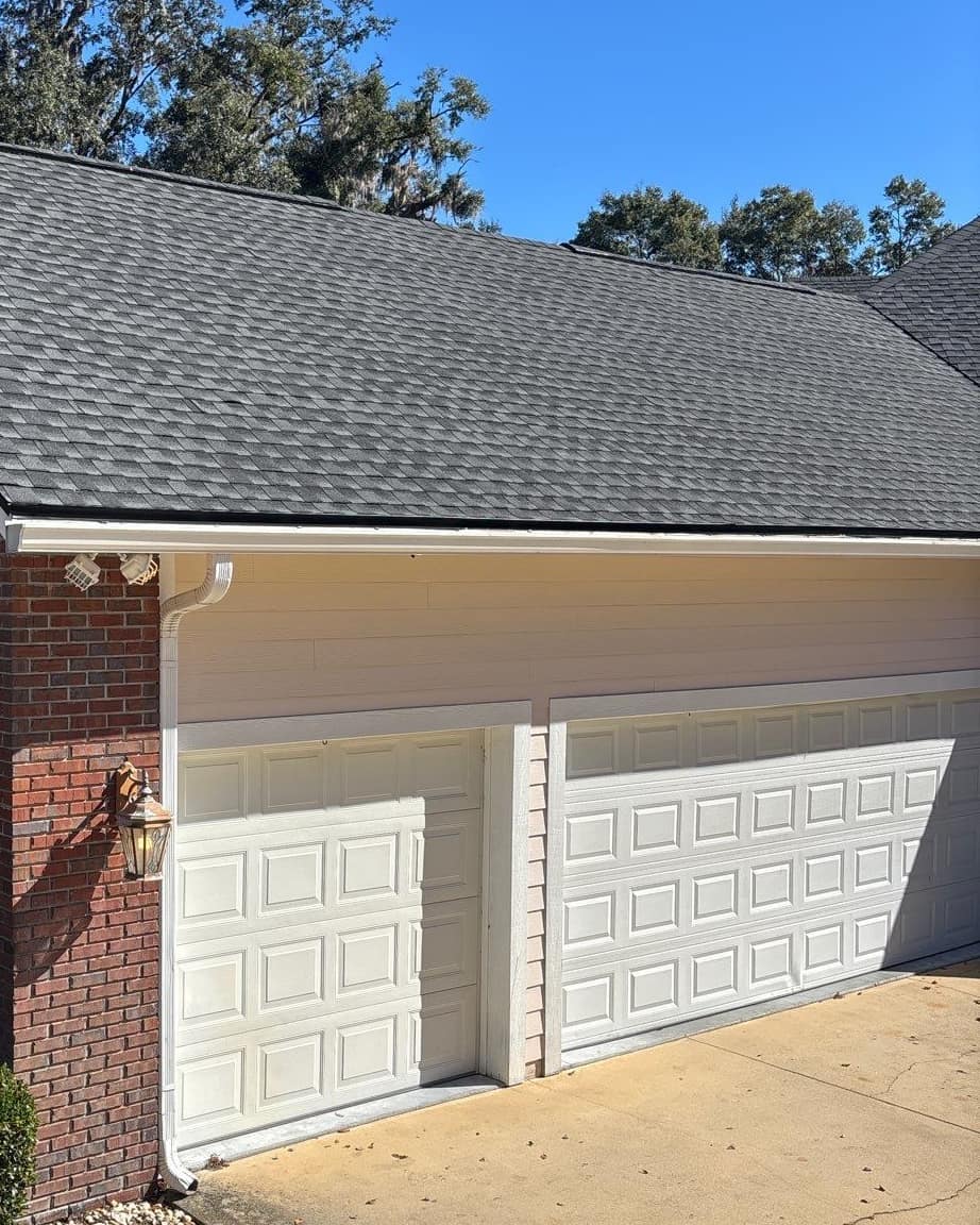 Garage wing roof above a brick corner, a coach lamp and two white garage doors in Newberry