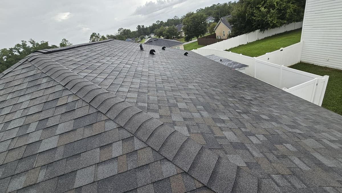 Hip cap shingles and black vent caps on the Newberry roof beside a white vinyl fence