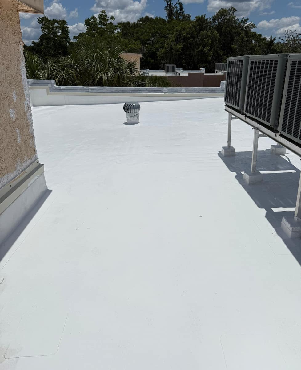 Second angle across the coated Ocala roof toward a stepped parapet, palms and a turbine vent
