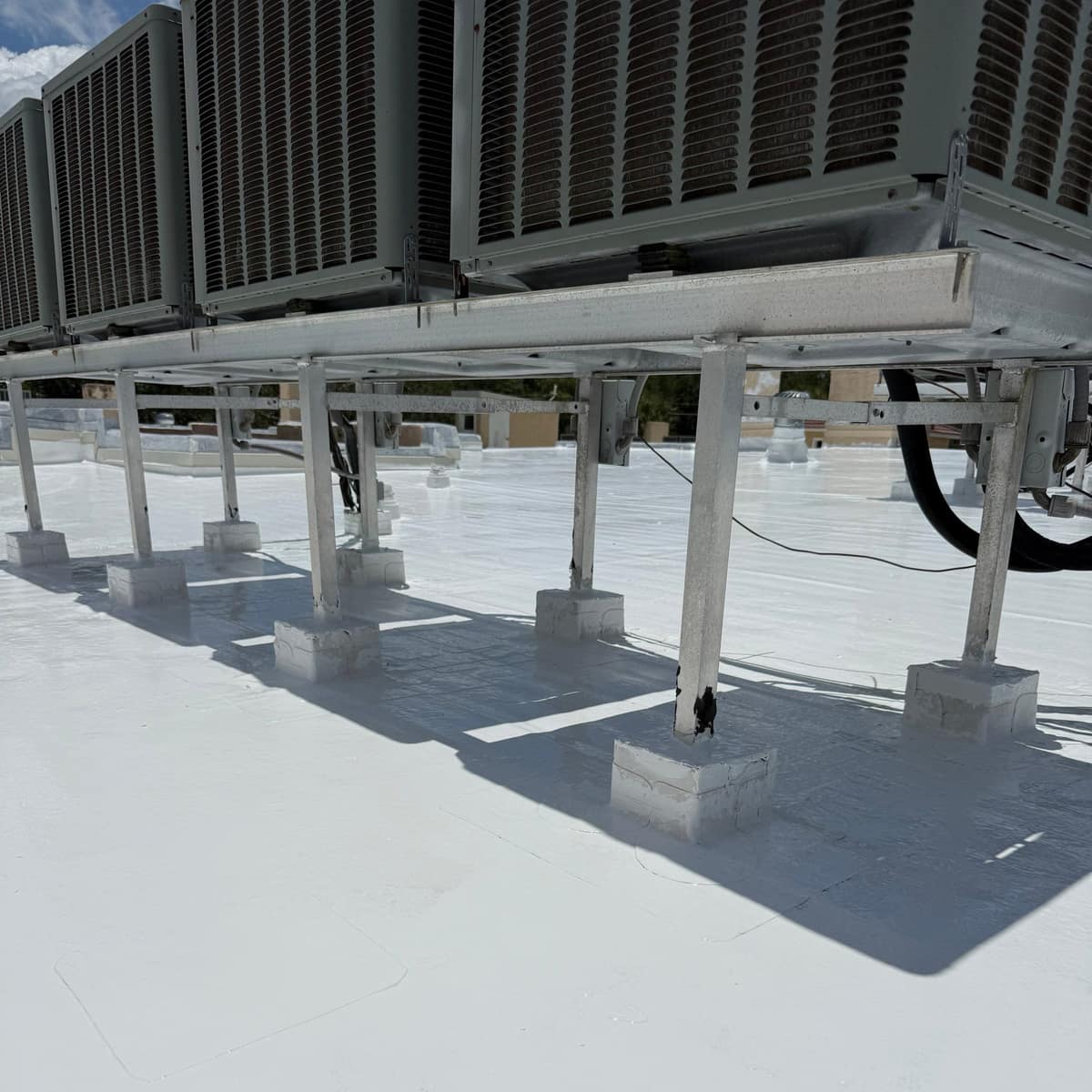 Metal AC rack legs standing in square boxes coated white on the Ocala roof