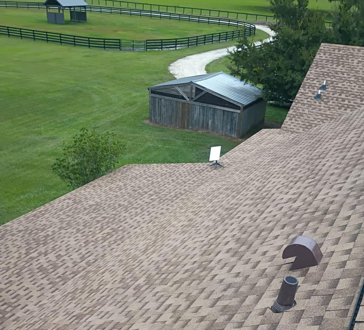 Back slope in Ocala with brown roof vents, a satellite dish and fenced pasture beyond