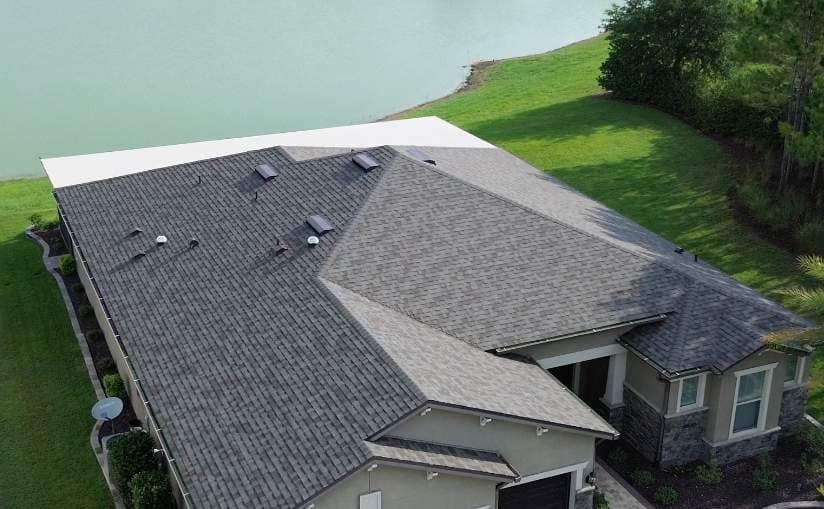 Drone view of a single-story Ocala home with a new gray and taupe shingle roof beside a lake