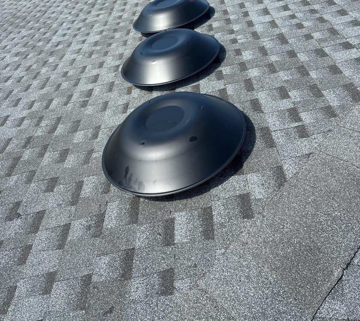 Three round black dome vents in a row on the new gray shingles in The Villages