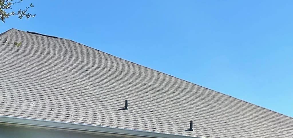 Looking up from the yard at a roof plane with two black vent stacks in The Villages